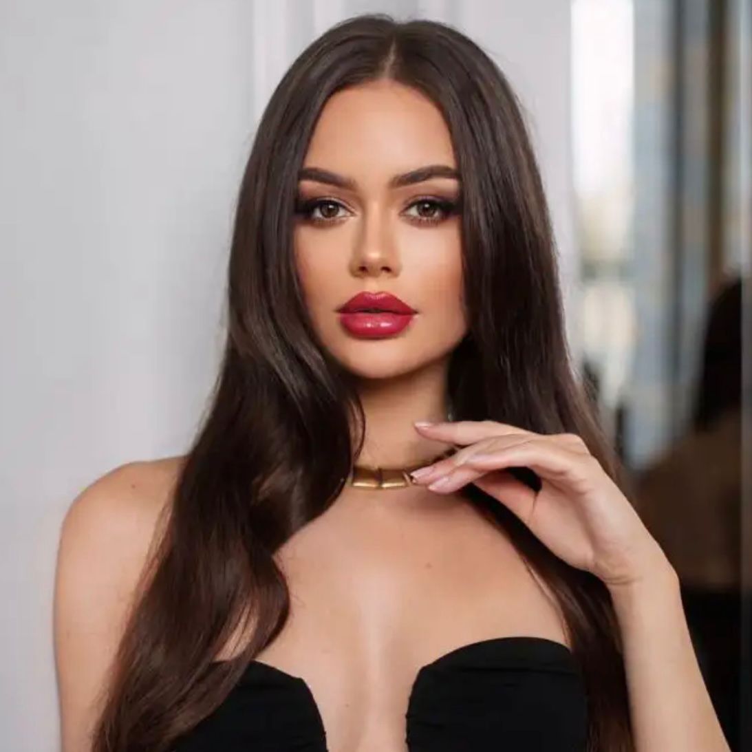 A naturally beautiful elite brunette escort wearing a black dress, gold necklace and a perfect face of make up