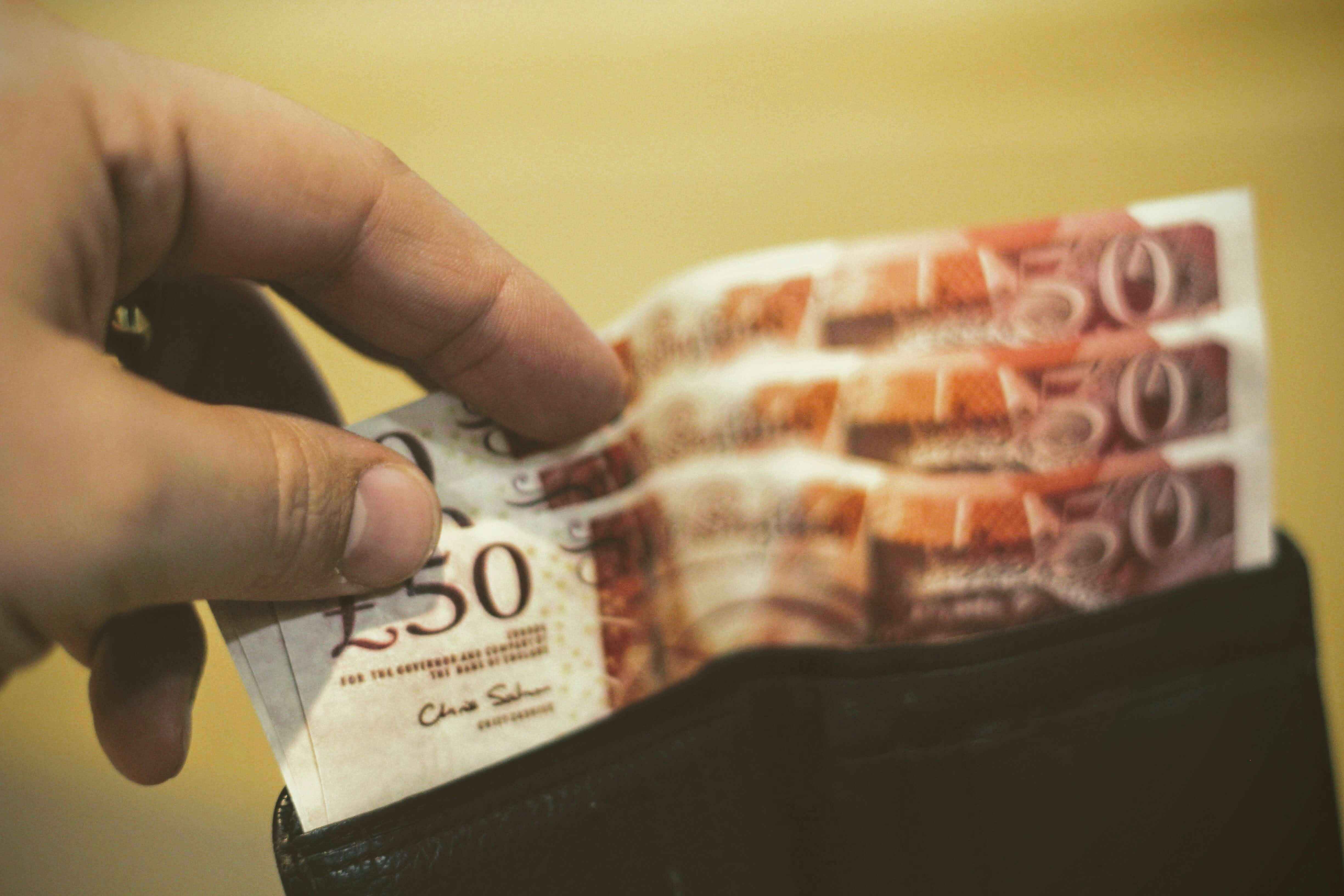 a man holding a wallet with 50 pound notes